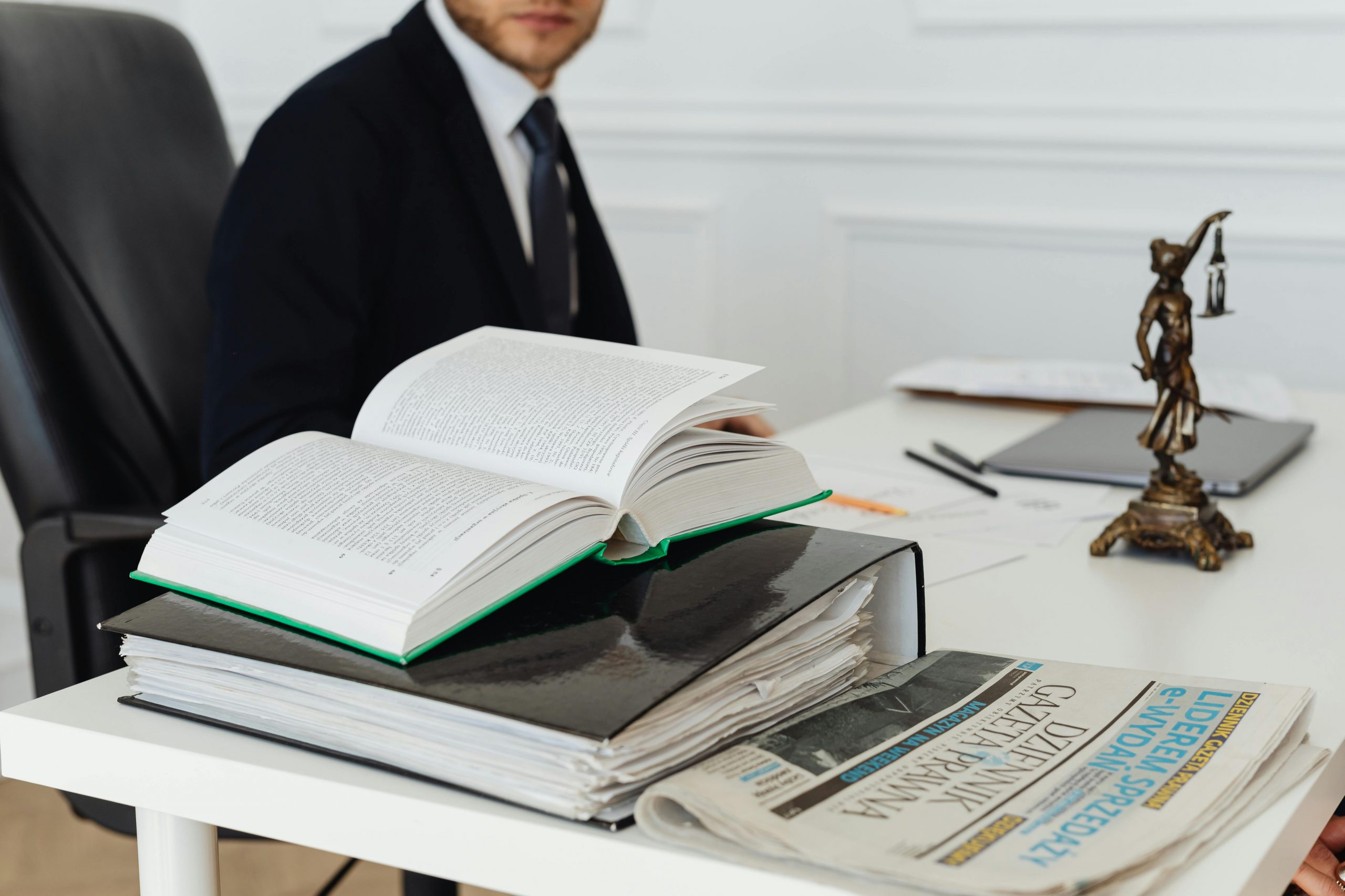 lawyer sitting at a desk with a binder, book, and Lady Justice figurine
