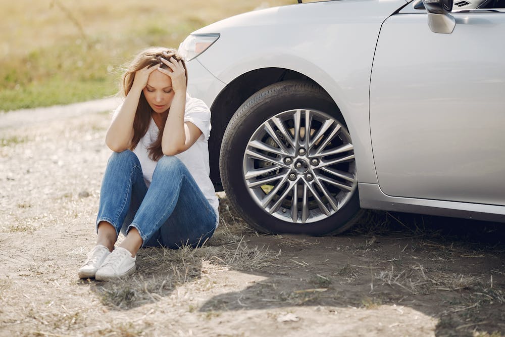 a frustrated woman sitting on the ground beside a car